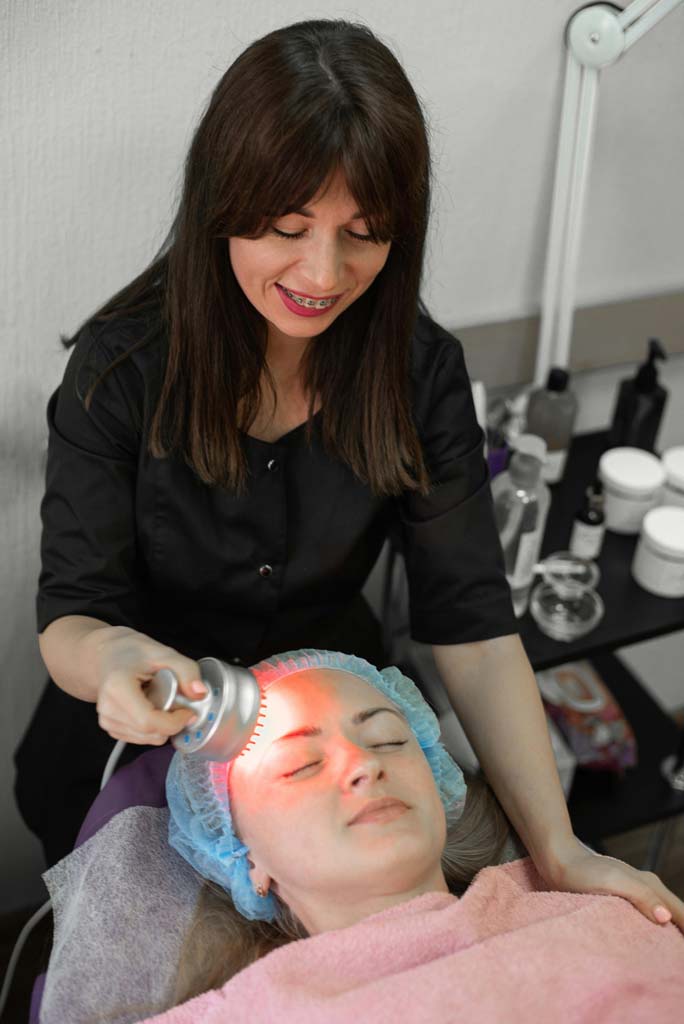A lady doing red light therapy on a female client